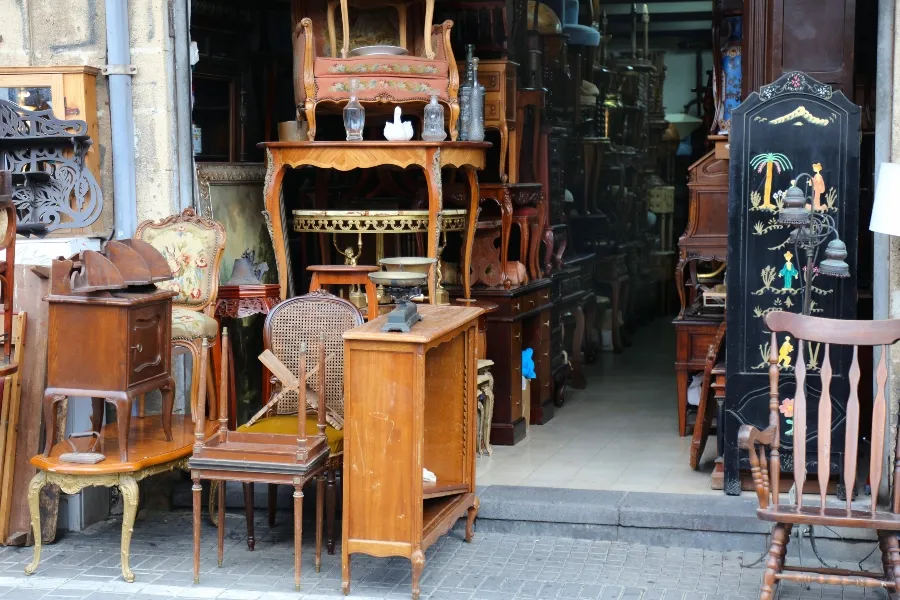 A crowded antique shop entrance displaying various used wooden furniture, chairs, tables, and a decorative screen on the sidewalk