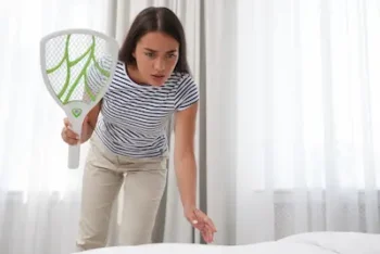 Young woman with electric fly swatter in bedroom, doing her own DIY pest control.